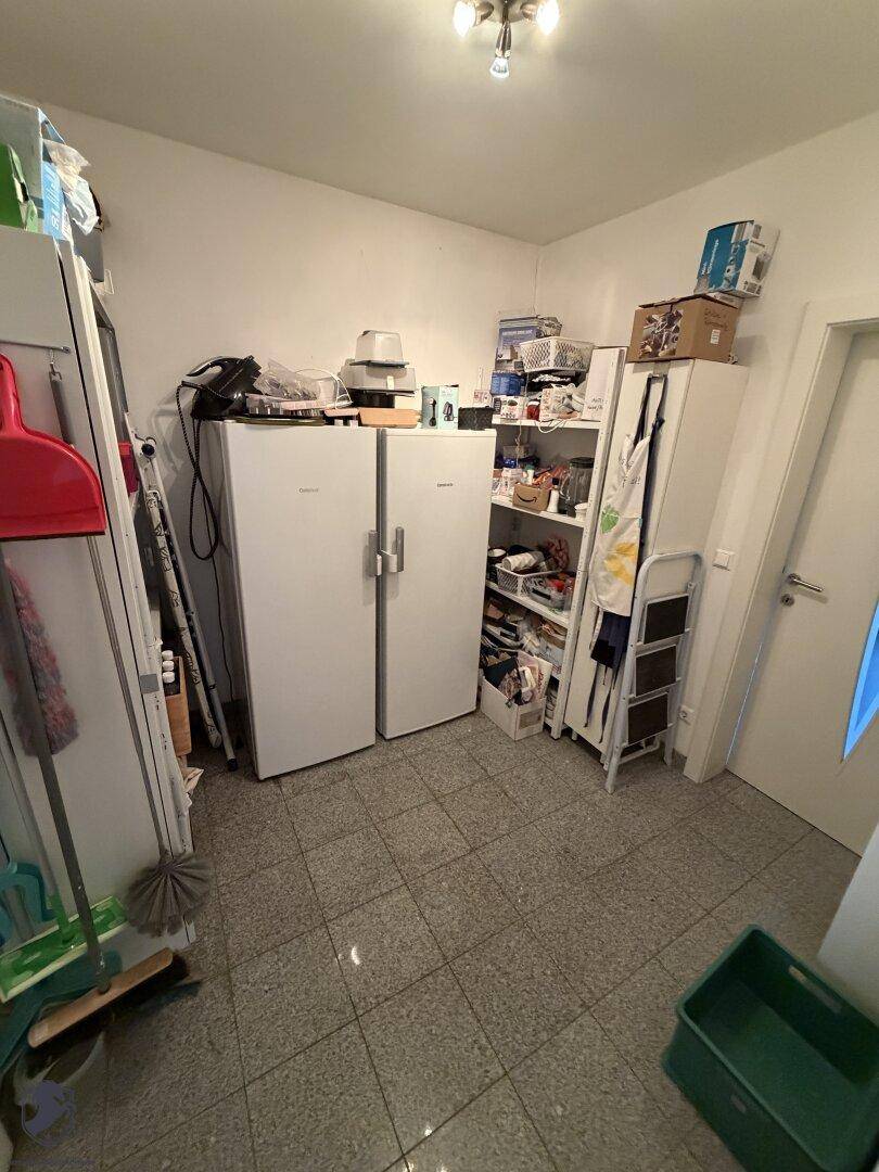 Praktischer Abstellraum mit zwei Kühlschränken, Regalen und Fliesenboden für zusätzlichen Stauraum.