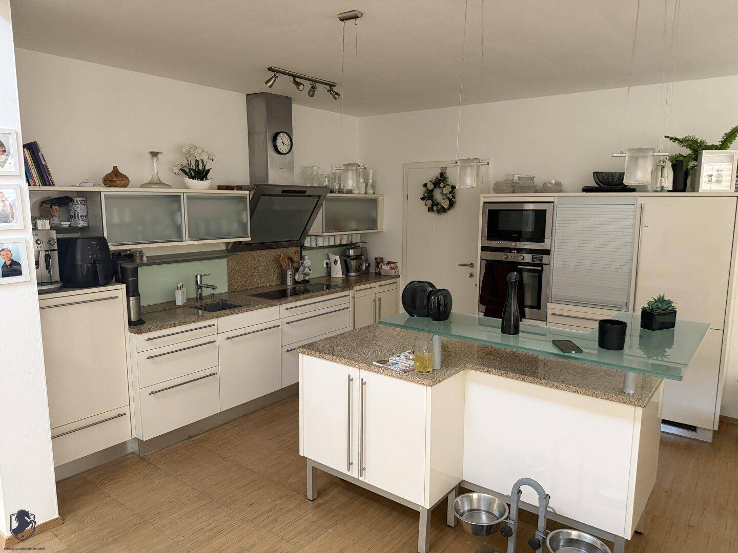 Moderne Küche mit weißen Schränken, Granitarbeitsplatten und einer Kücheninsel mit Glasaufsatz.