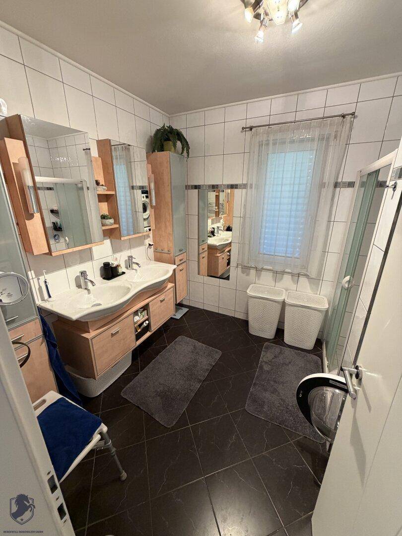 Badezimmer mit dunklen Fliesen, Doppelwaschbecken, Spiegelschränken und einer Duschkabine.