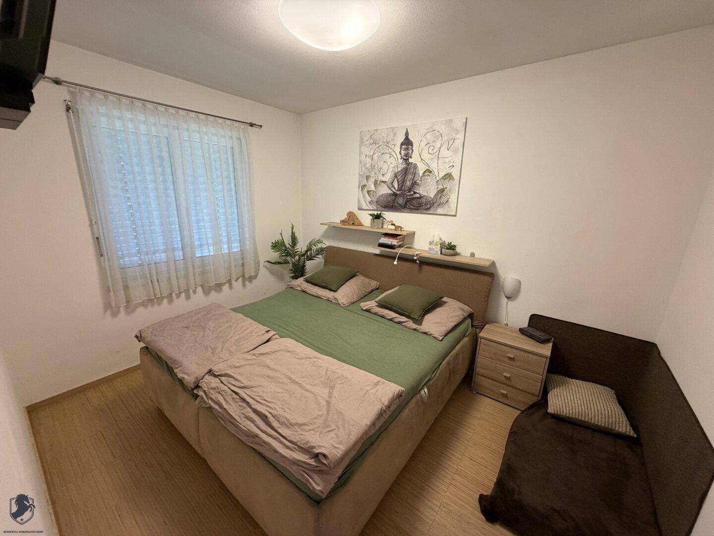 Schlafzimmer mit Doppelbett, Nachttisch und einem Fenster, dekoriert mit einem Buddha-Bild.