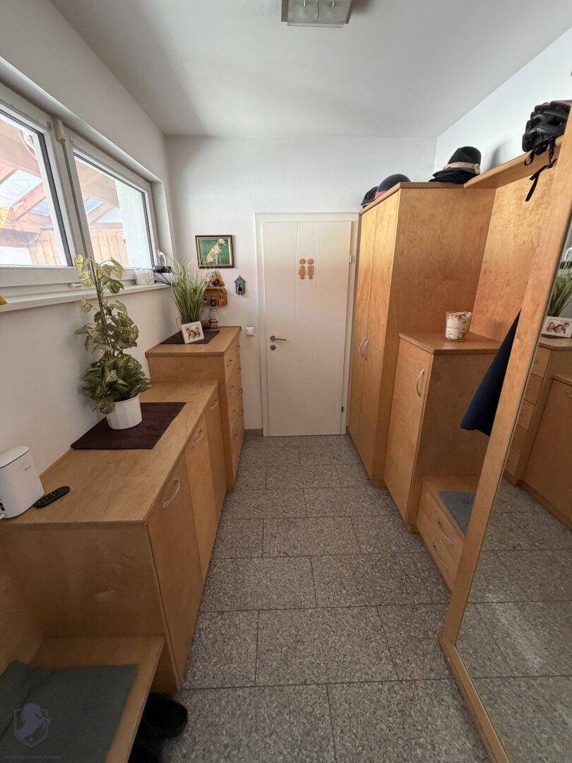 Eingangsbereich mit Fliesenboden, Holzschränken, einem Spiegel und einem Fenster.