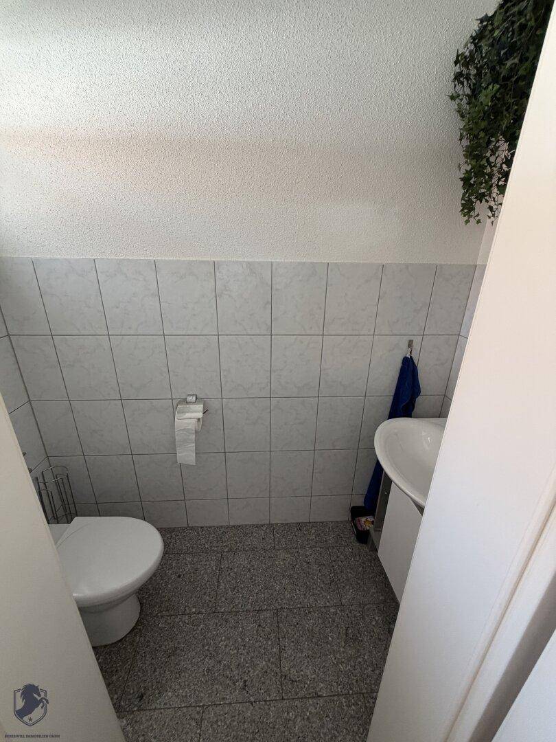Kleines Gäste-WC mit weißer Toilette, Waschbecken und hellen Fliesen an Wänden und Boden.