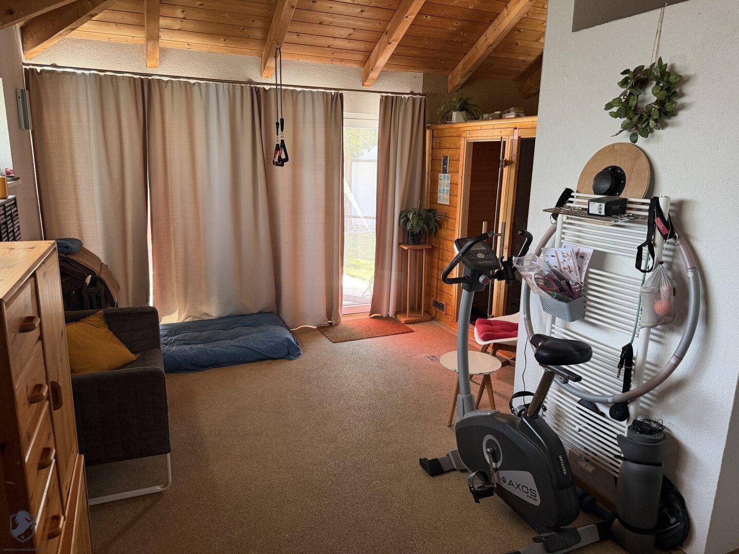 Fitnessraum mit Sauna, Trainingsgeräten und Zugang zum Außenbereich unter Holzdecken.