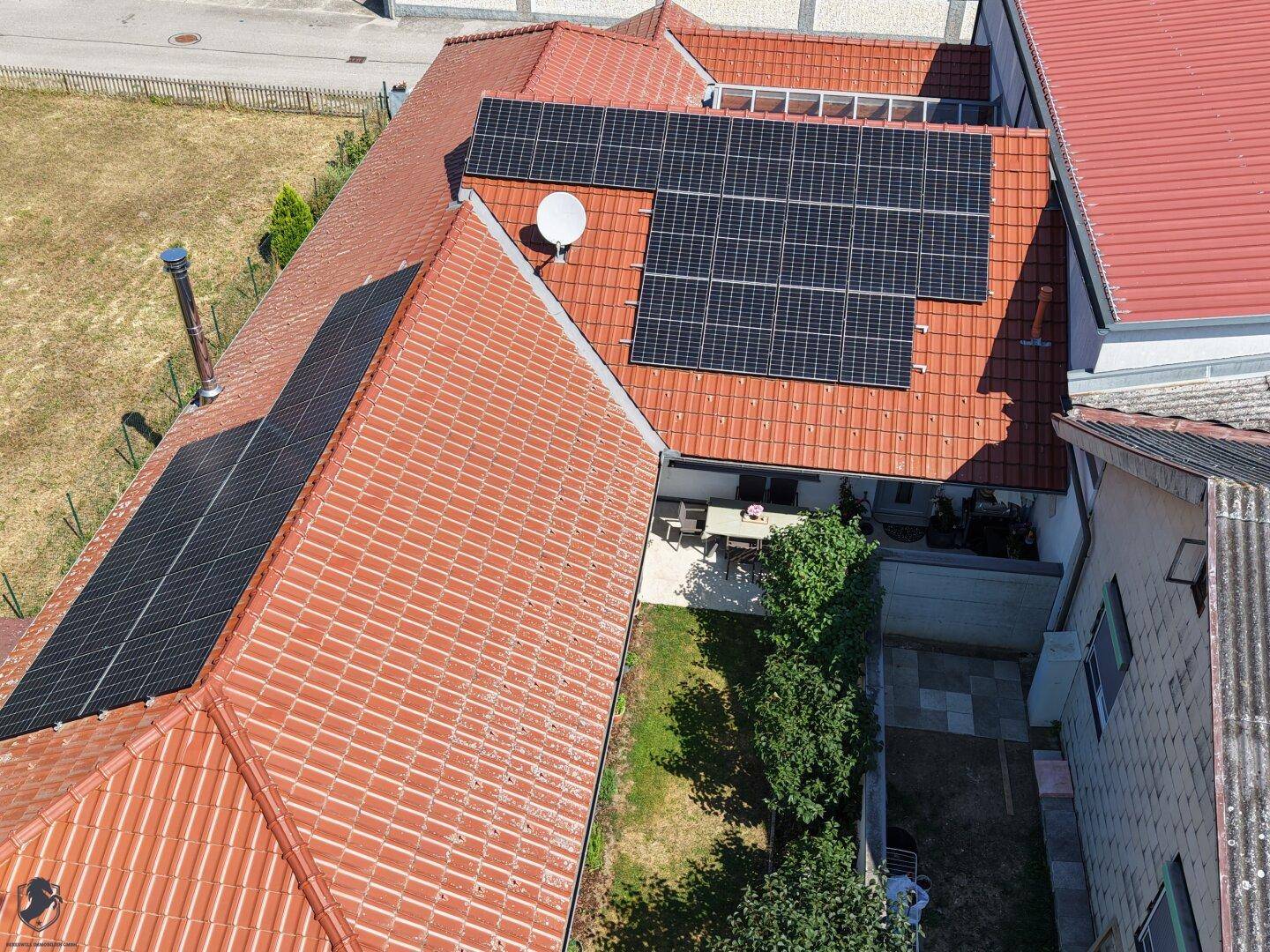 Dach mit Solaranlagen und einem gemütlichen Essbereich im Freien, umgeben von Grün.