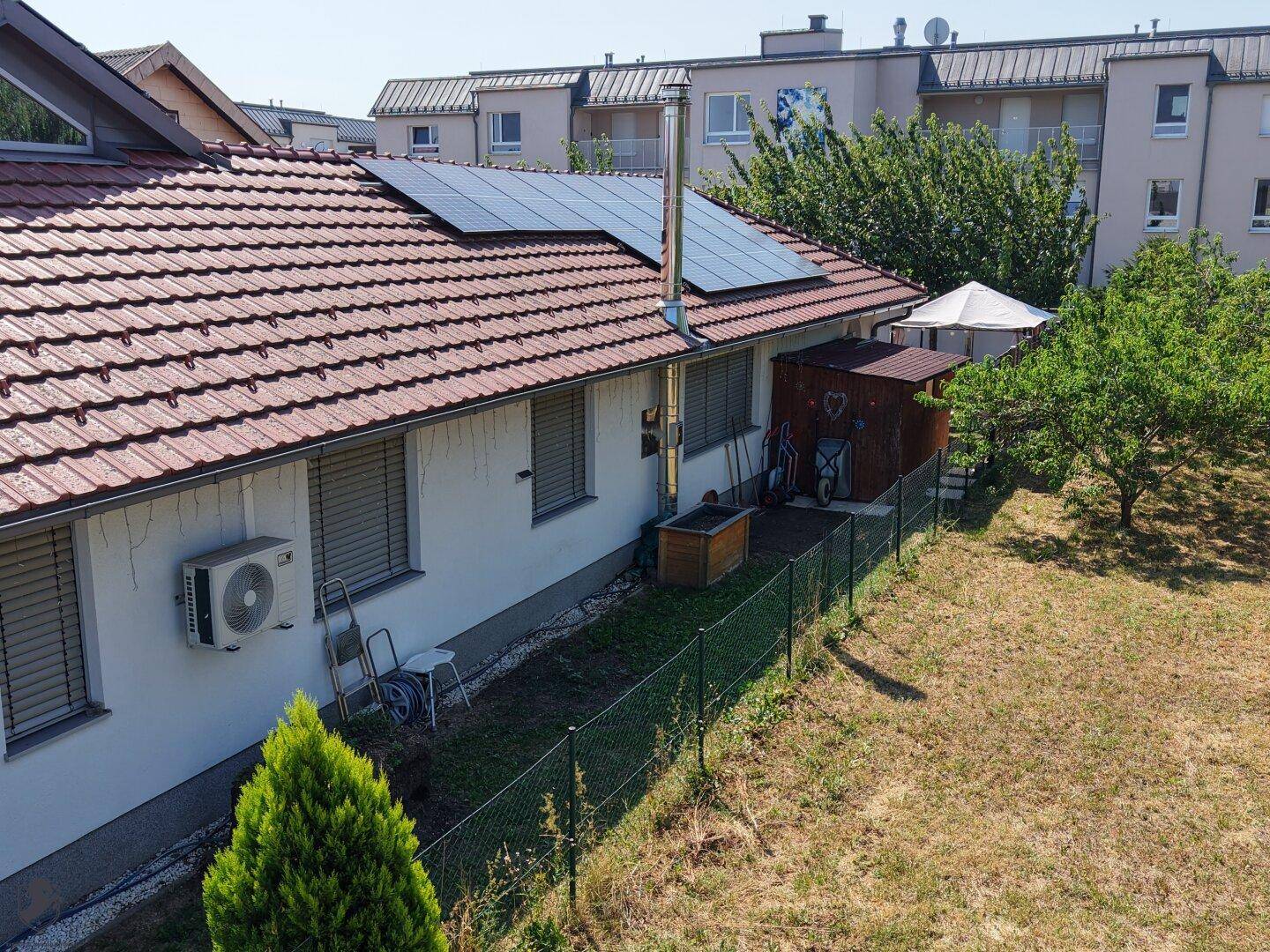 Luftaufnahme der Hausseite mit Solarpaneelen auf dem Dach, Klimaanlage und Gartenschuppen.