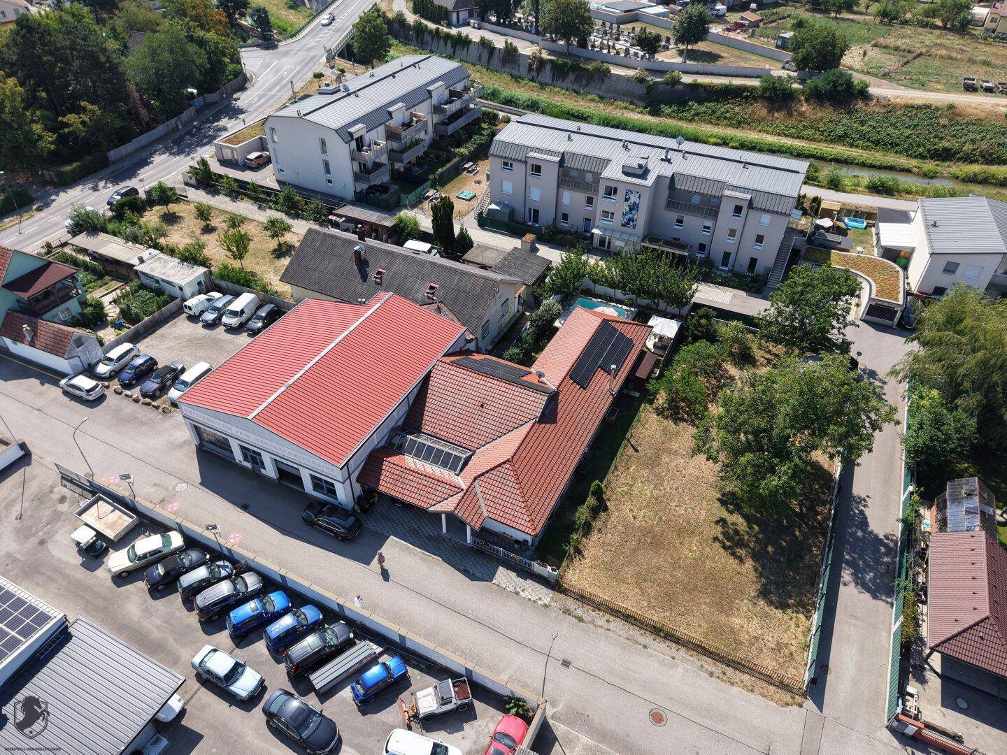 Luftaufnahme eines Anwesens mit mehreren Gebäuden, Parkplätzen und Solaranlagen auf den Dächern.