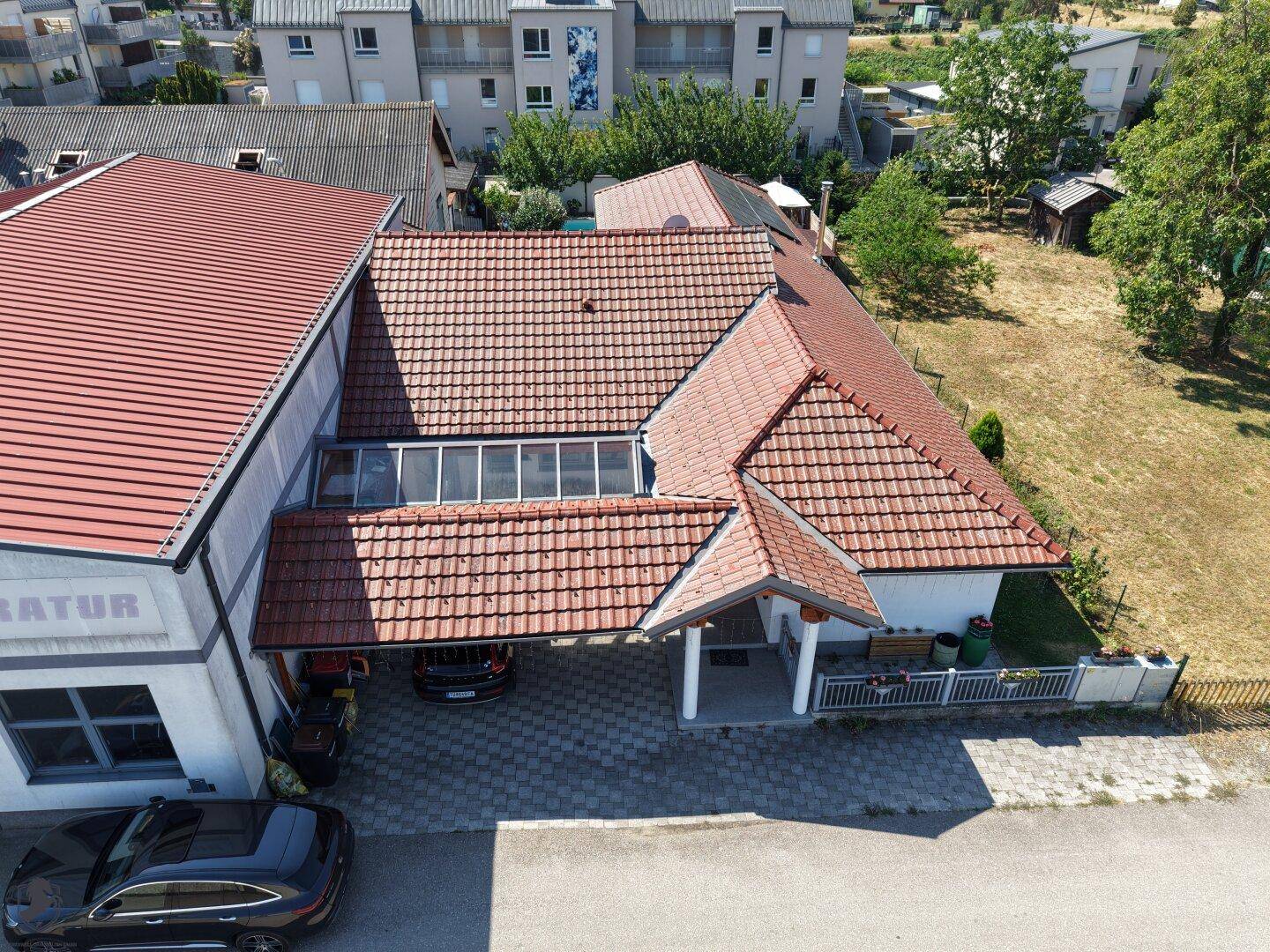 Luftaufnahme des Anwesens mit Fokus auf das Haus und seine Dachstruktur, umgeben von Gebäuden.