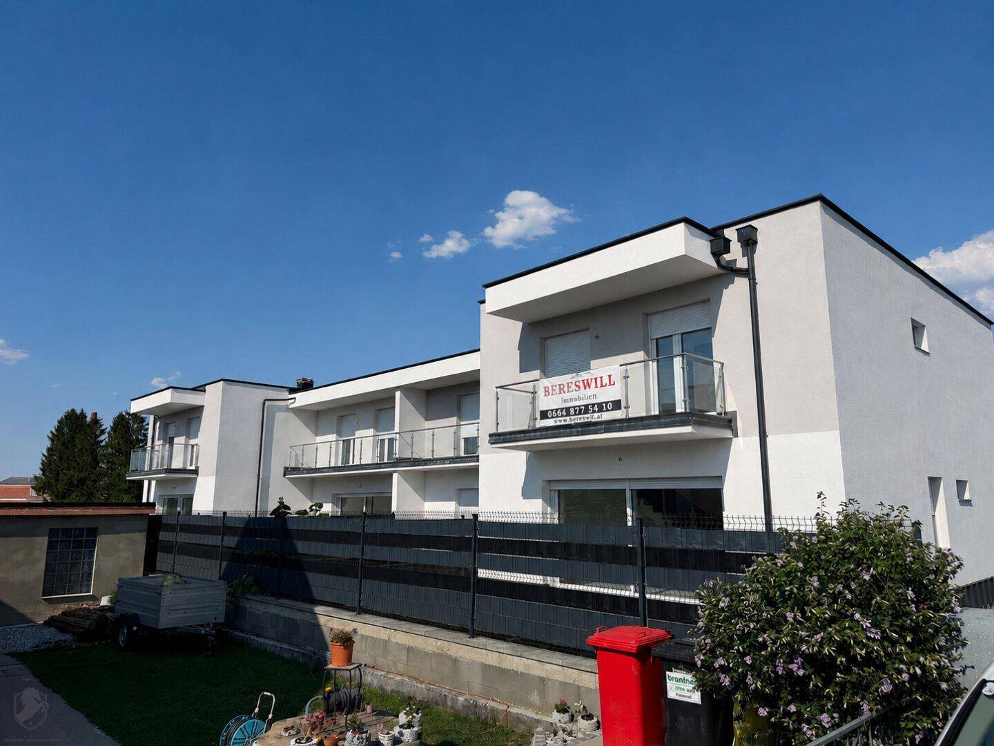 Moderne Fassade eines Neubaus mit Balkonen und einem "Zu verkaufen"-Schild unter blauem Himmel.