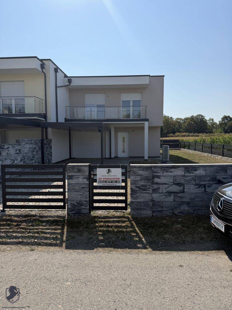 Neubau-Reihenhaus mit modernem Design, kleinem Vorgarten und einem "Zu verkaufen"-Hinweis.