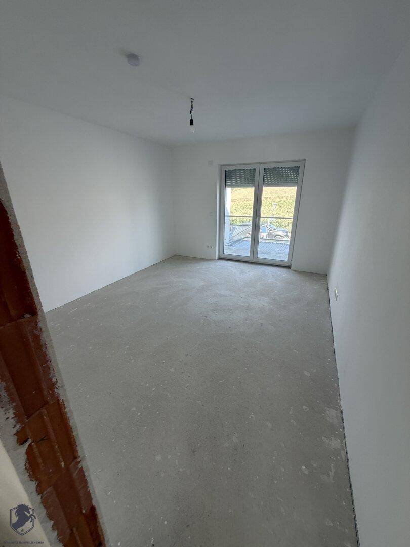 Helles Schlafzimmer im Rohbau mit weiß gestrichenen Wänden und Blick auf die grüne Umgebung.