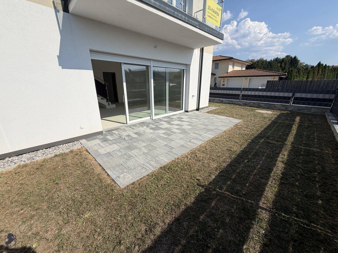 Hinterhof mit gepflasterter Terrasse, Rasenfläche und großen Glasschiebetüren zum Wohnbereich.