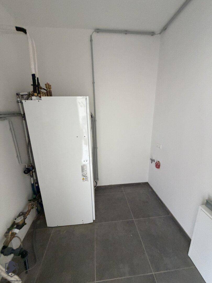 Hauswirtschaftsraum mit Wärmepumpe und dunkelgrauen Fliesen, bereit für den Erstbezug.