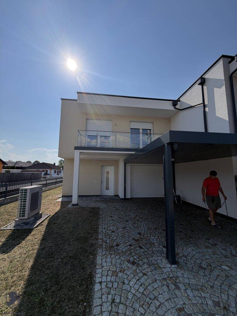 Vorderansicht des Neubaus mit Carport, Eingangsbereich und Außeneinheit der Wärmepumpe.
