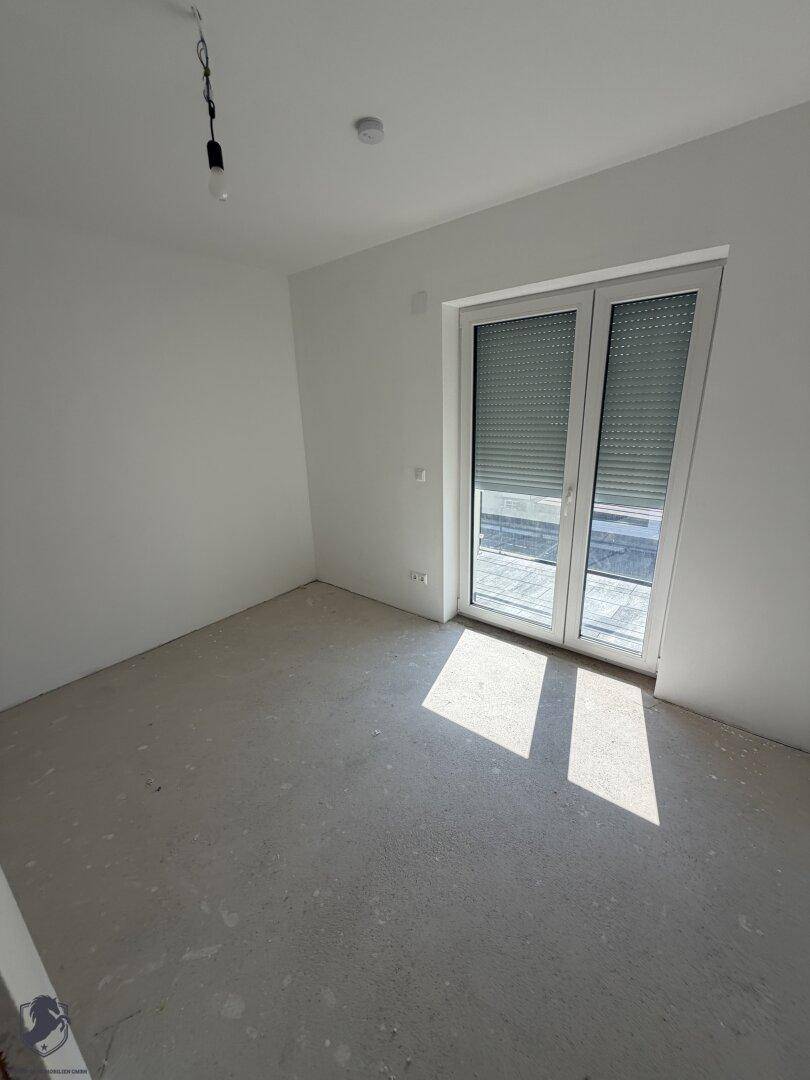 Lichtdurchflutetes Schlafzimmer im Rohbau mit weißer Grundierung und Blick nach draußen.