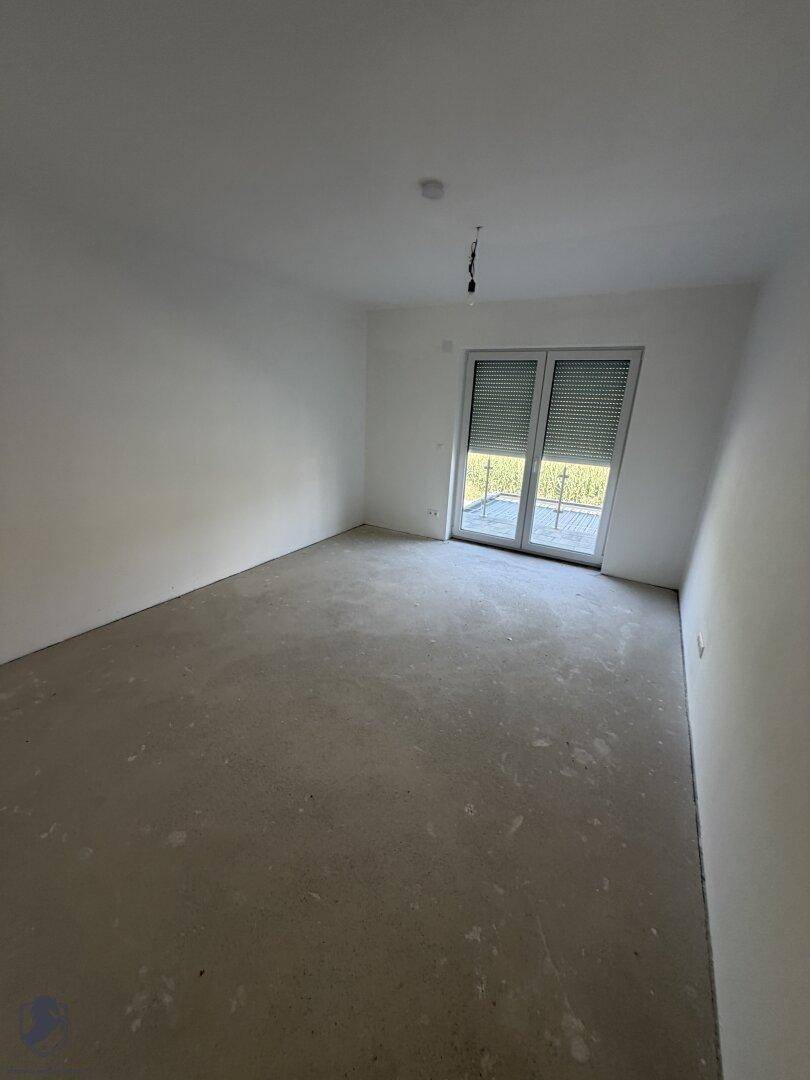 Helles Schlafzimmer im Rohbau mit weiß gestrichenen Wänden und Blick auf die grüne Umgebung.