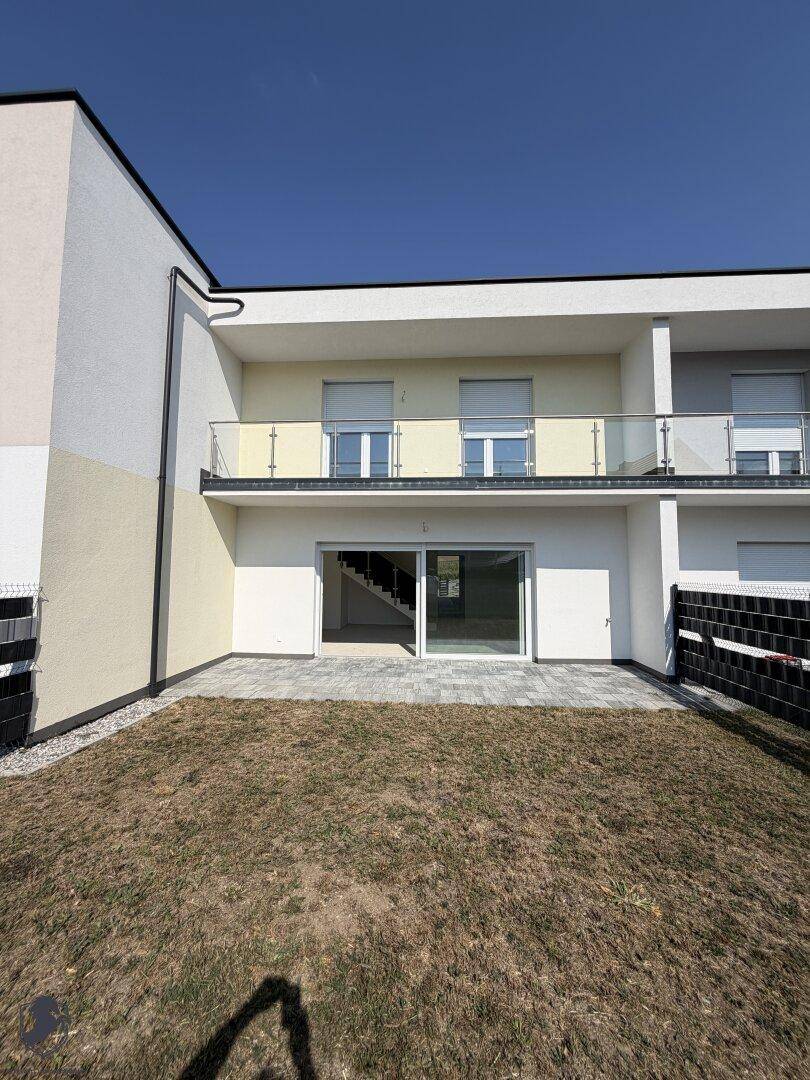 Hinterhof mit gepflasterter Terrasse, Rasenfläche und großen Glasschiebetüren zum Wohnbereich.