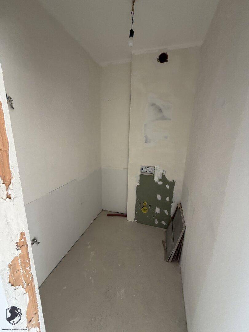 Kleiner, unfertiger Raum mit weißen Wänden und sichtbaren Installationen, ideal als Abstellraum.