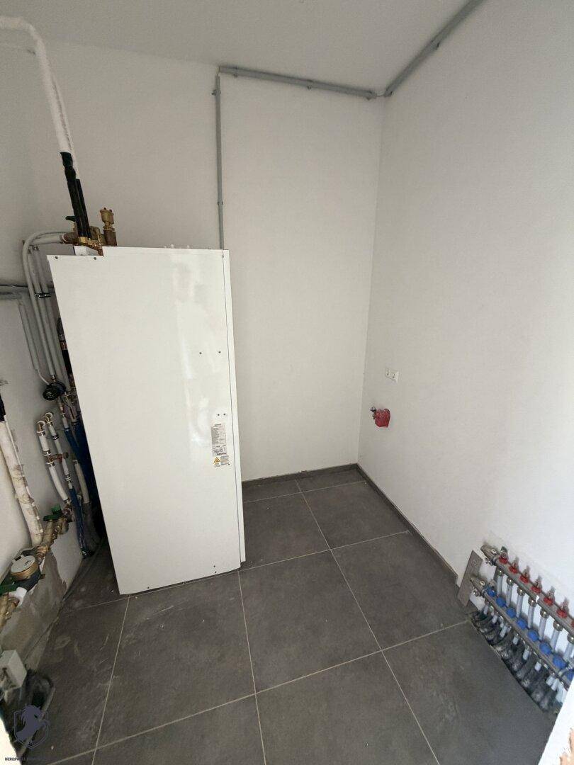 Hauswirtschaftsraum mit Wärmepumpe, Fliesenboden und sichtbaren Rohrleitungen.