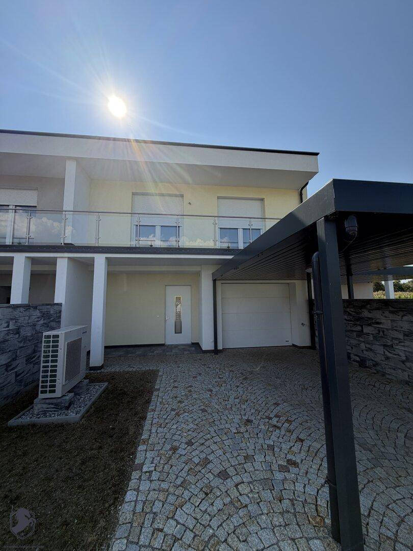 Moderne Hausfassade mit Carport, gepflasterter Auffahrt und Balkon im Obergeschoss.