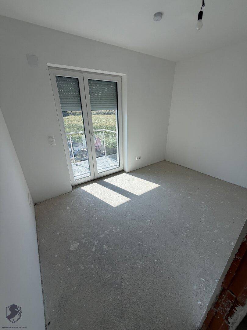Helles, unfertiges Zimmer mit Rohbetonboden und weitem Blick ins Grüne.