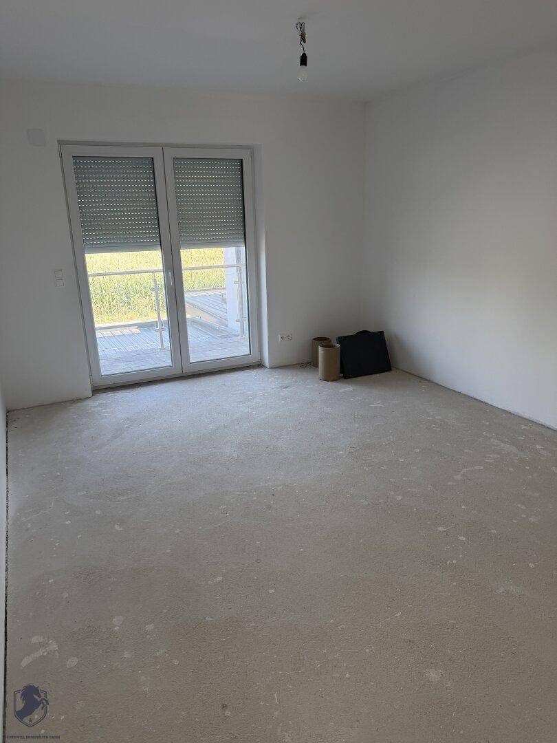 Helles, unfertiges Zimmer mit Rohbetonboden und großen Fenstern für viel Tageslicht.
