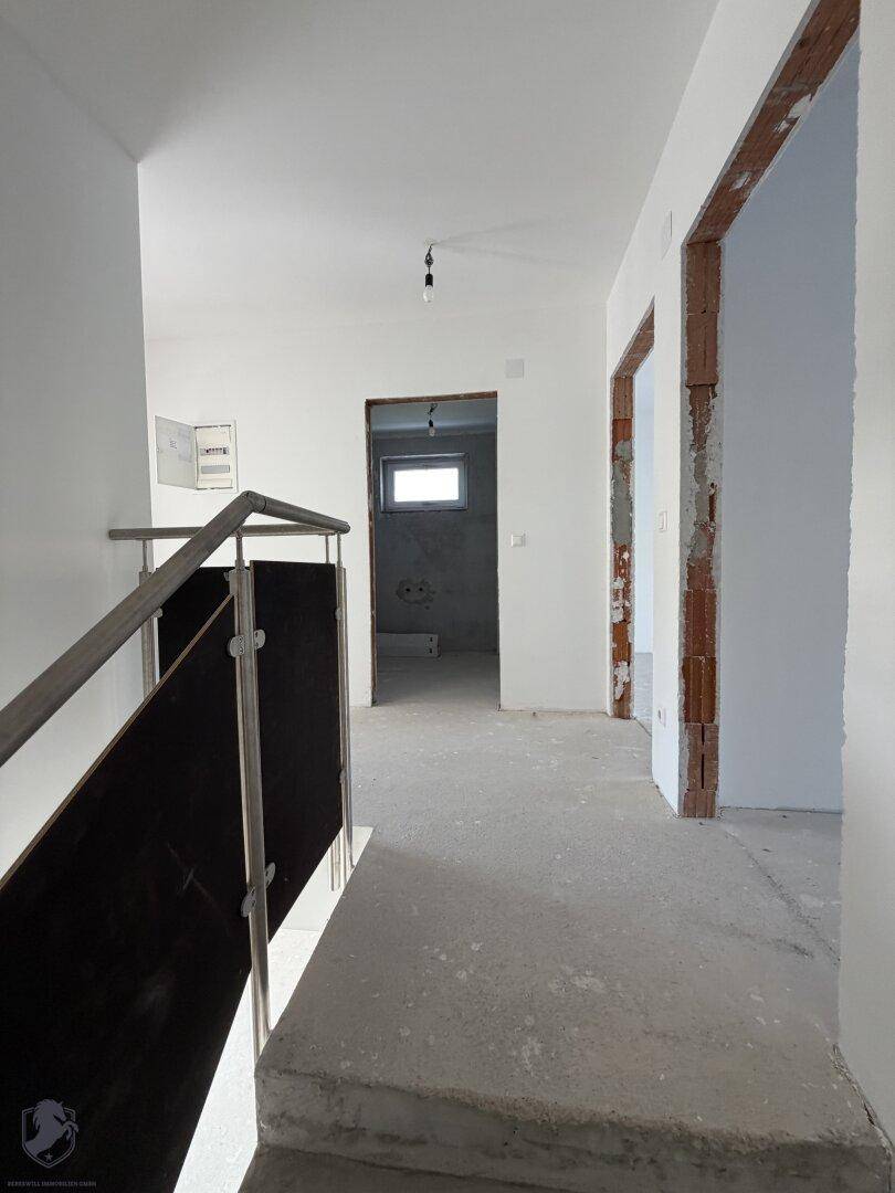 Unfertiger Flur im Obergeschoss mit Treppengeländer und Blick auf ein kleines Fenster.