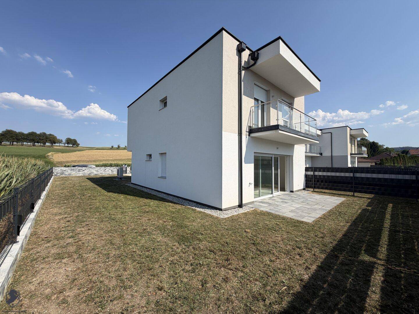 Moderne Hausrückseite mit gepflasterter Terrasse, Garten und weitem Blick ins Grüne.