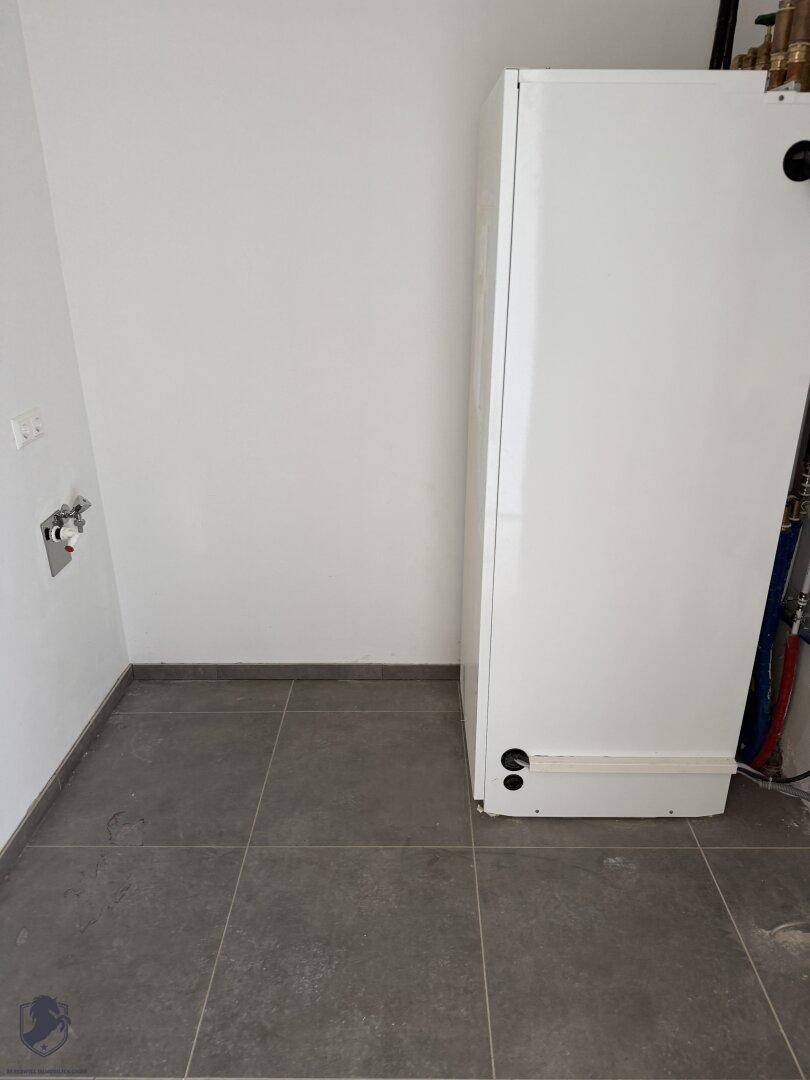 Detailansicht der Wärmepumpe im Hauswirtschaftsraum mit dunklem Fliesenboden.