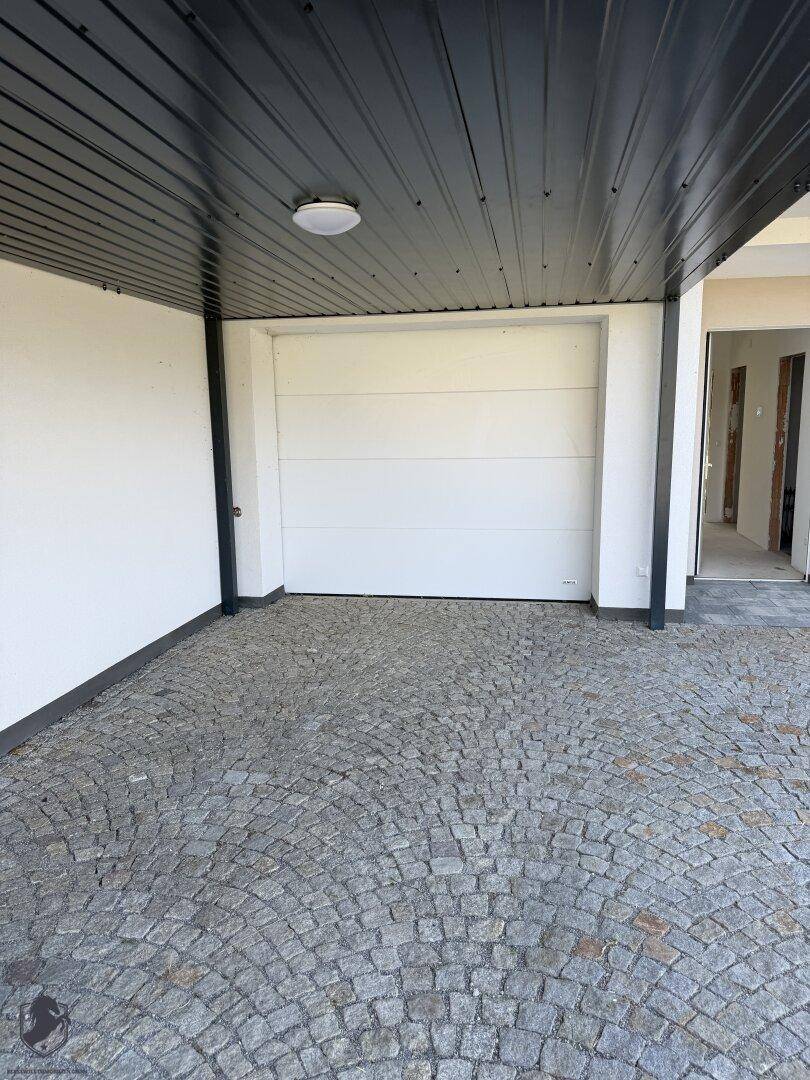 Überdachter Carportbereich mit gepflasterter Auffahrt und Garagentor.