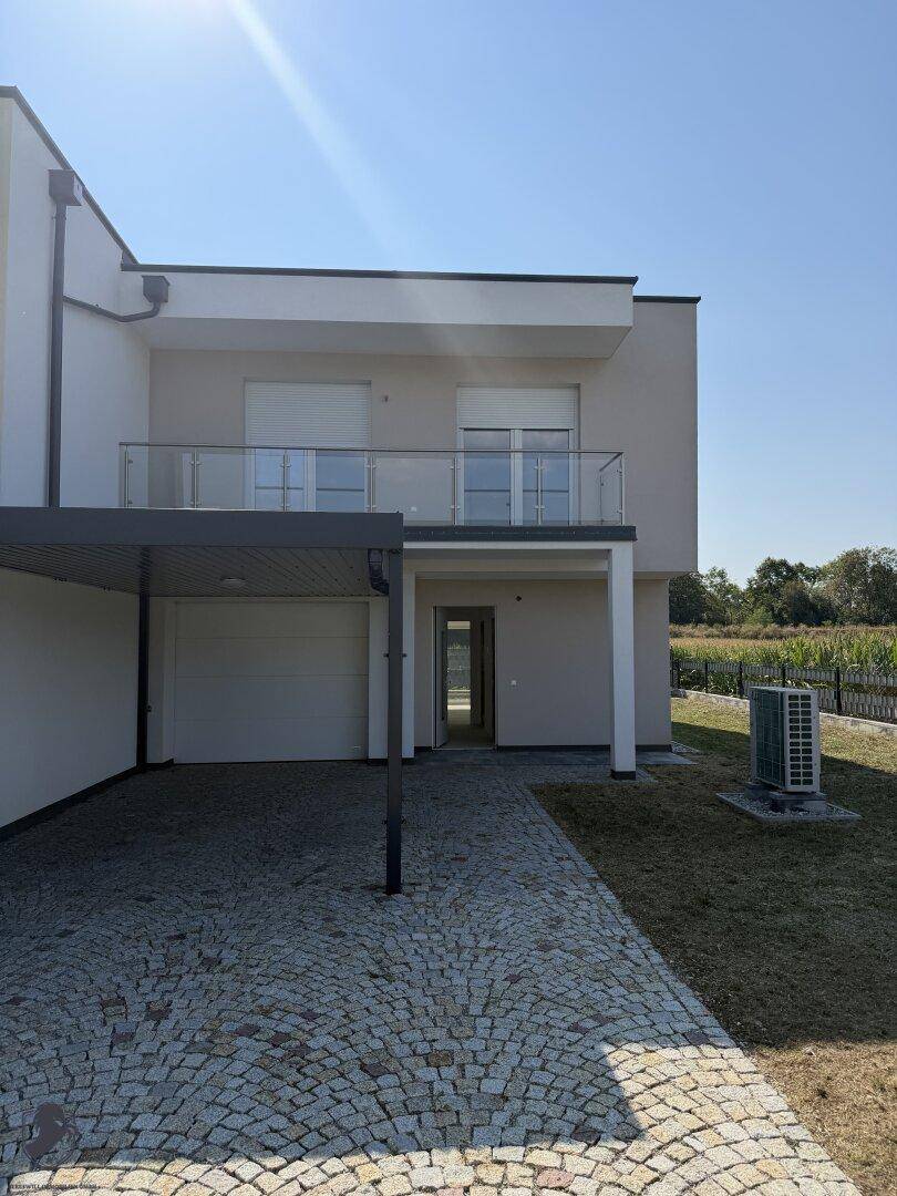 Moderne Hausfassade mit Carport, gepflasterter Auffahrt und kleinem Vorgarten.
