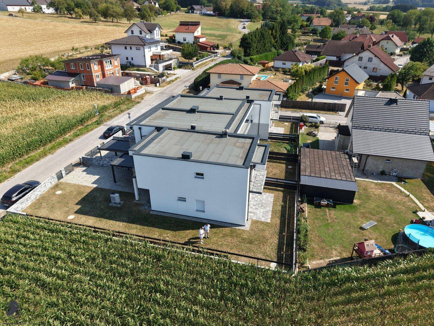 Neubau-Reihenhäuser mit Flachdächern und angrenzenden Feldern unter blauem Himmel, mit Carports.