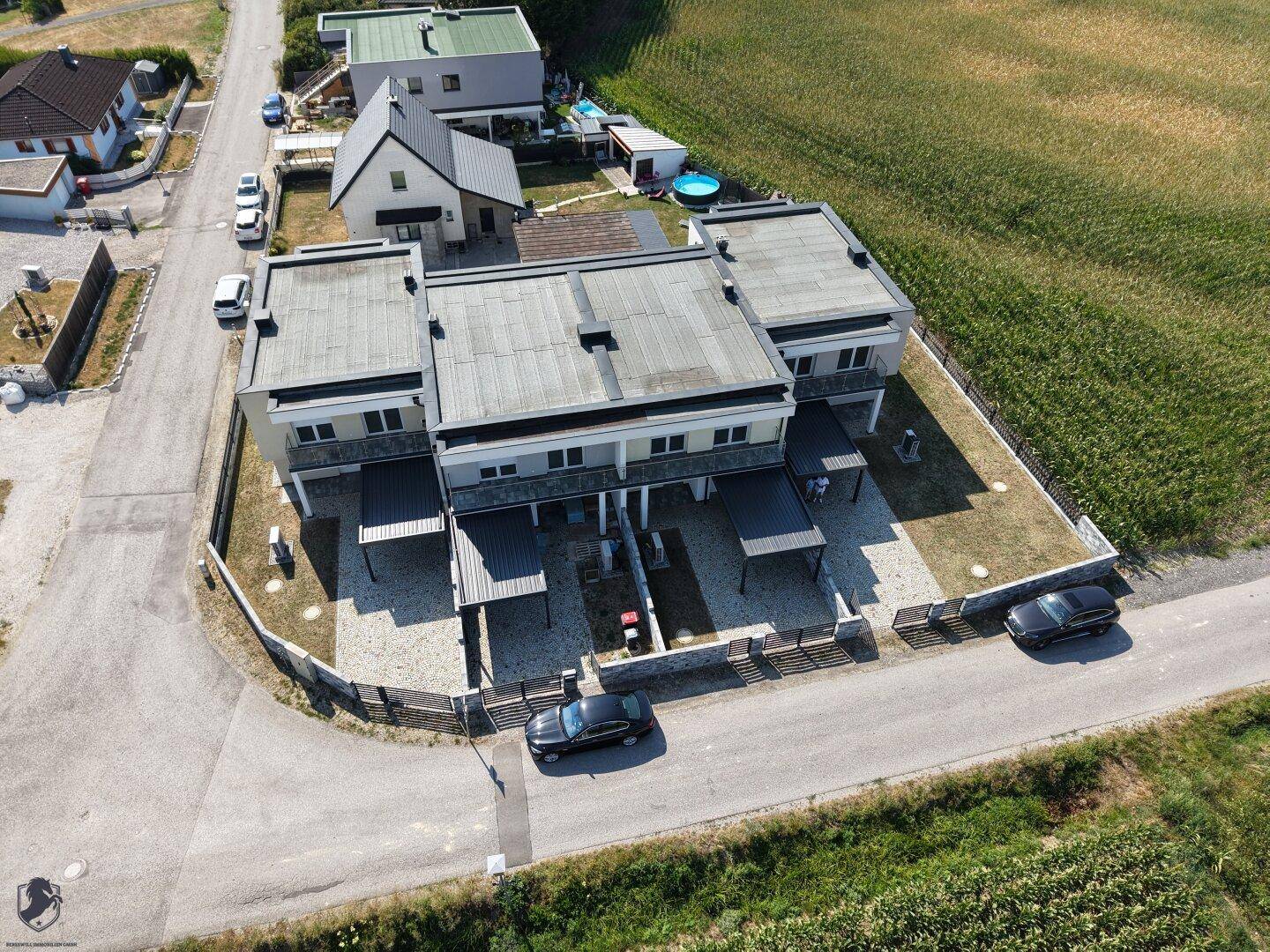 Reihenhäuser mit modernen Flachdächern und Carports, umgeben von ländlicher Landschaft und Straßen.
