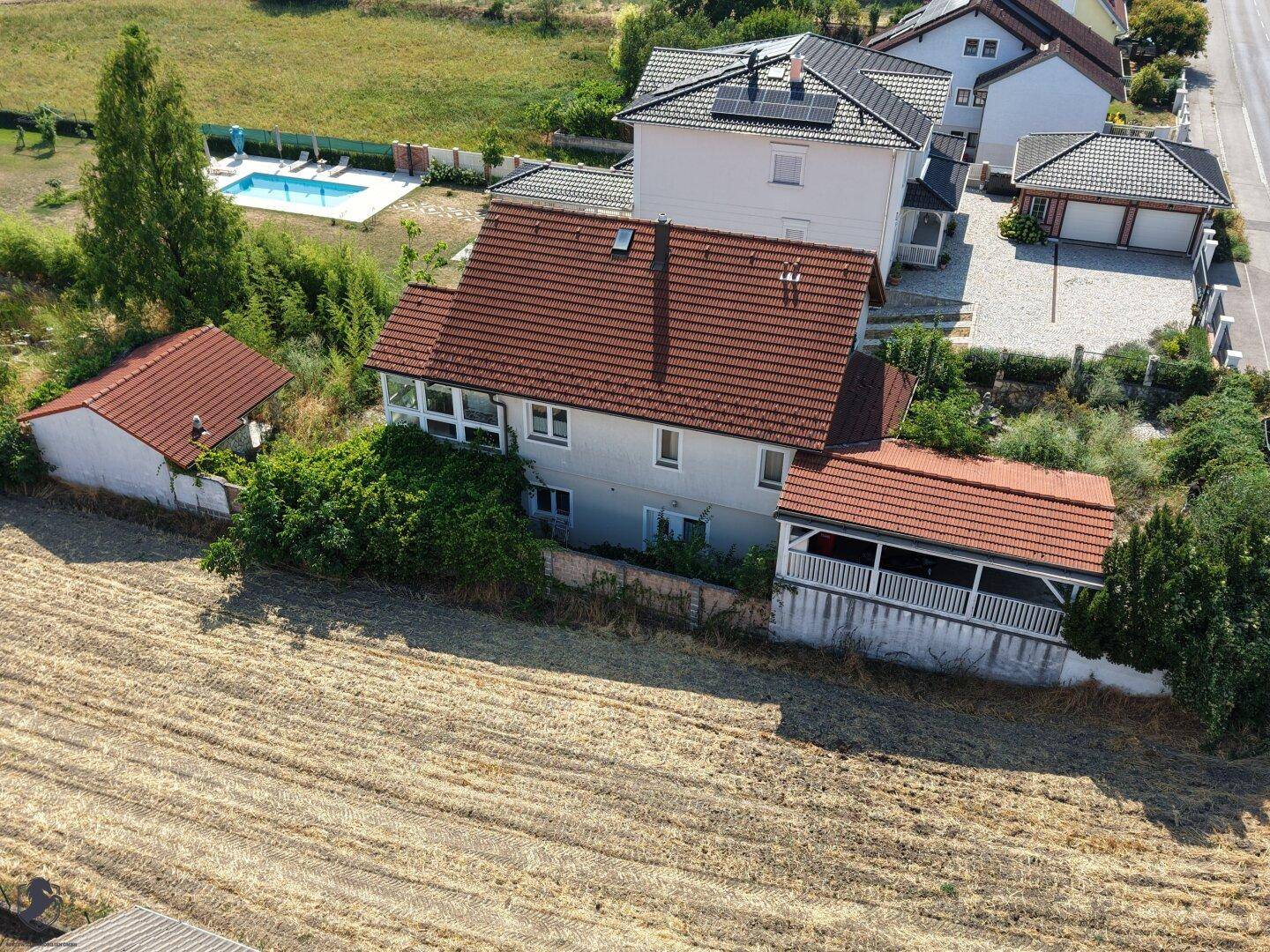 Rückansicht des Hauses aus der Luft, mit einem Pool in der Nachbarschaft und weiten Feldern.