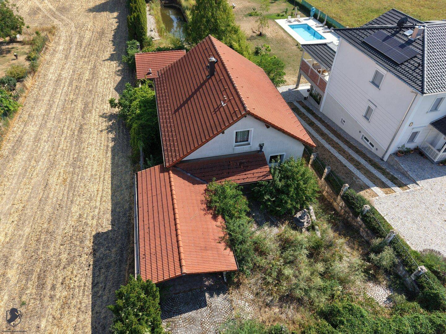 Seitenansicht des Hauses aus der Luft mit Carport, verwildertem Gartenbereich und angrenzendem Feld.