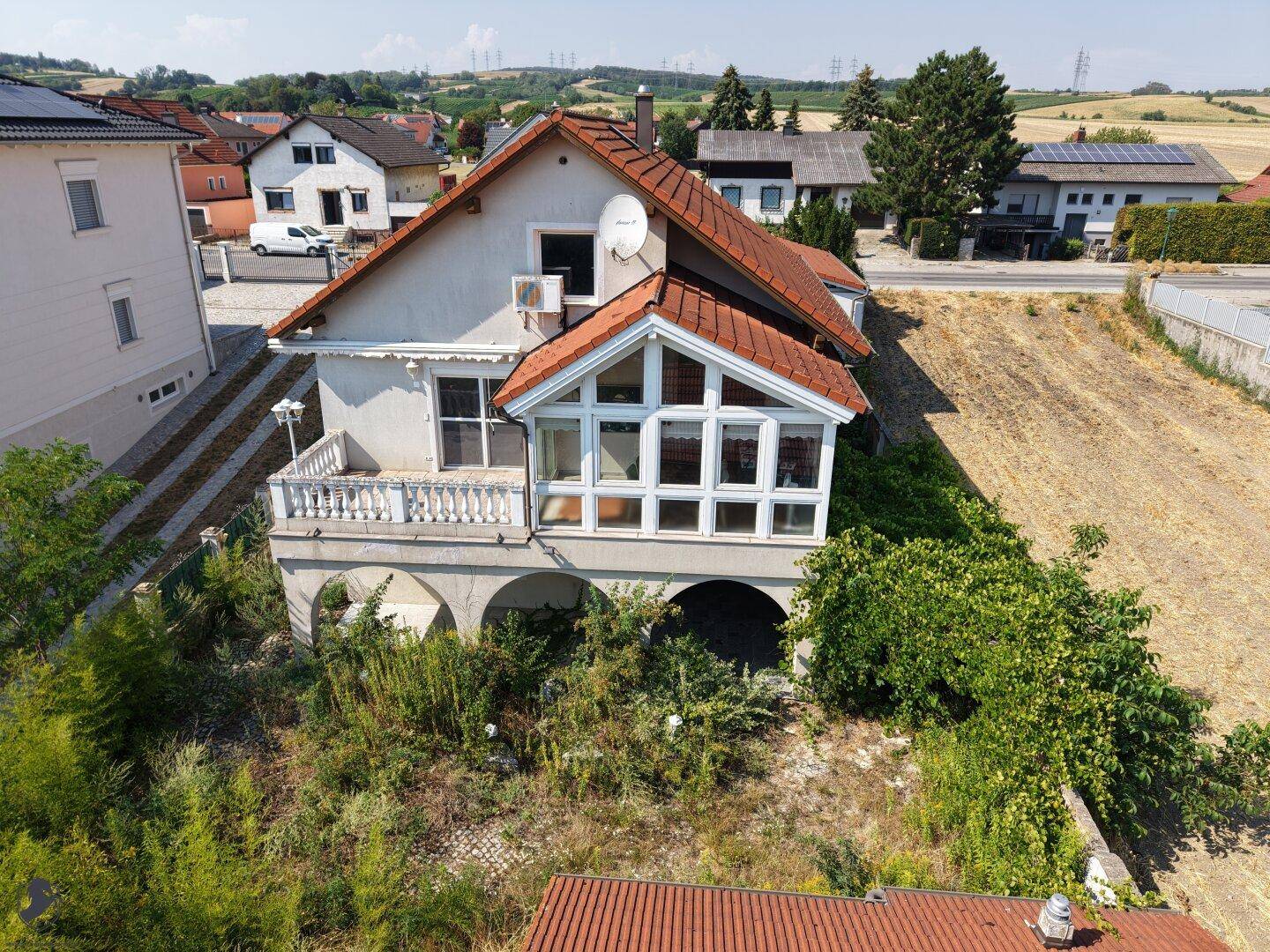 Ansicht eines Hauses mit rotem Ziegeldach, weißer Fassade, Balkon und einem verglasten Wintergarten.