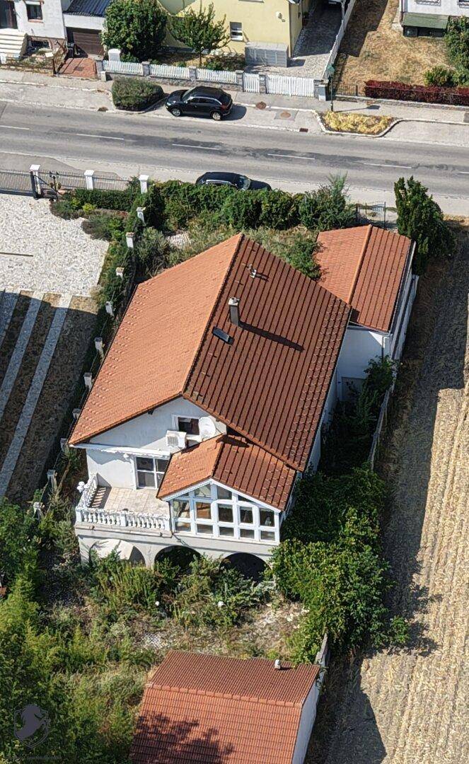 Vogelperspektive des Hauses mit rotem Ziegeldach, angrenzender Straße und einem weiten Feld.