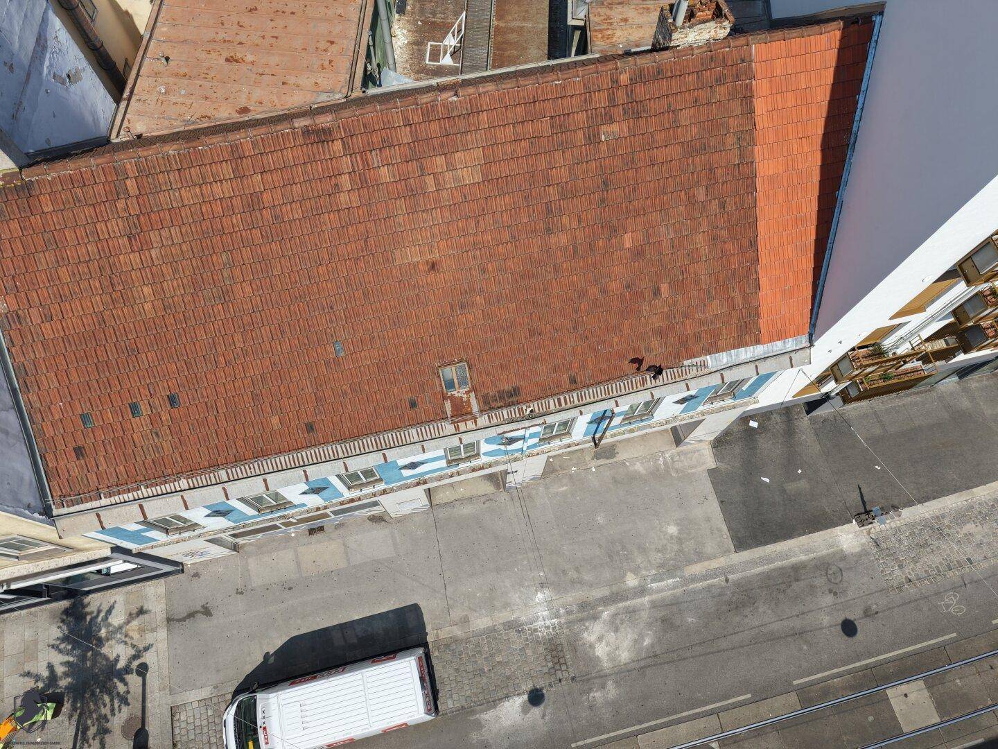 Direkte Luftaufnahme des Gebäudes mit Ziegeldach und der darunterliegenden Straße mit Fahrzeugen.