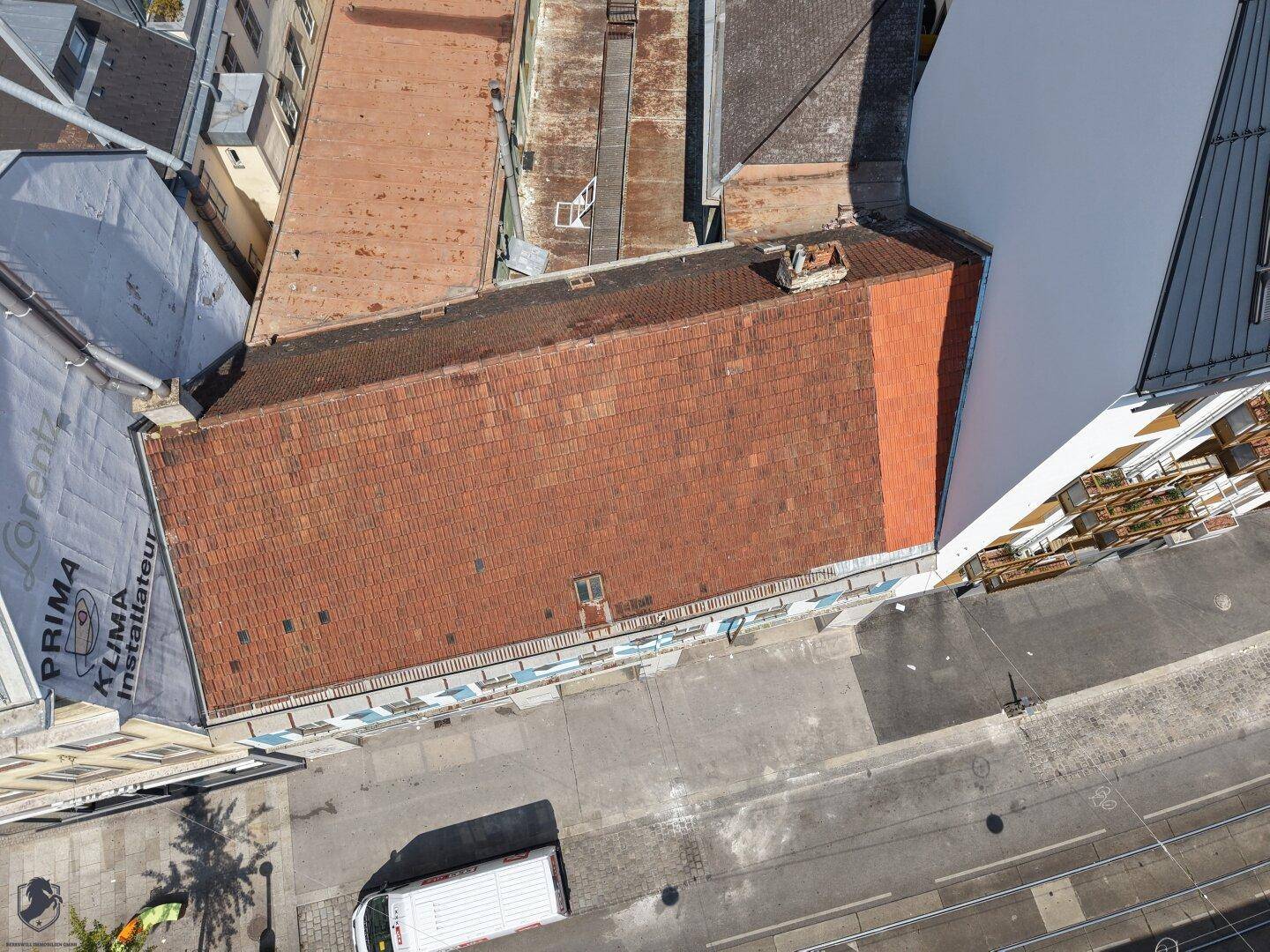 Luftaufnahme des Gebäudes mit rotem Ziegeldach und der belebten Straße davor.