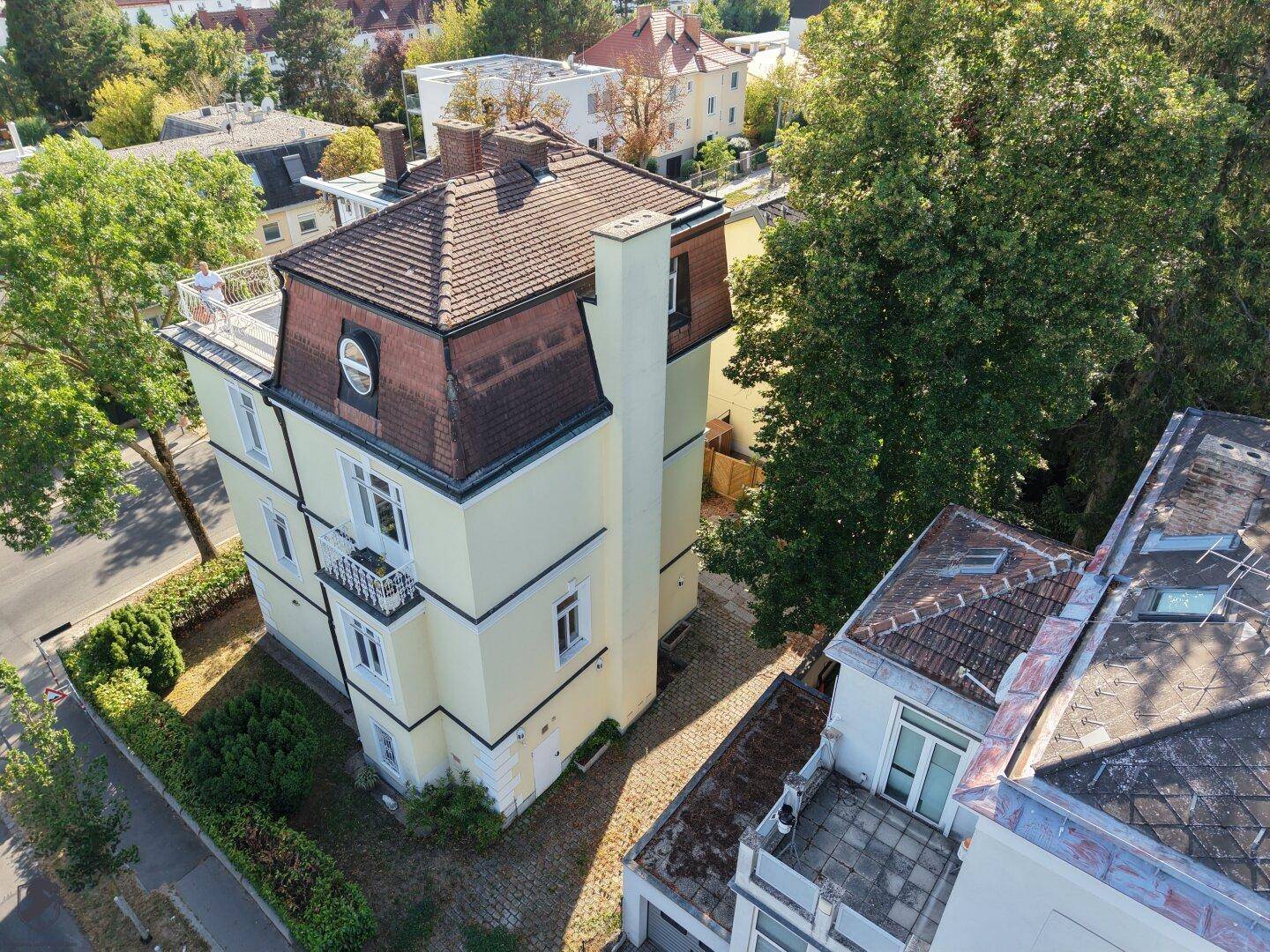 Seitliche Luftaufnahme des Gebäudes mit gelber Fassade, Mansarddach und angrenzenden Nachbarhäusern.