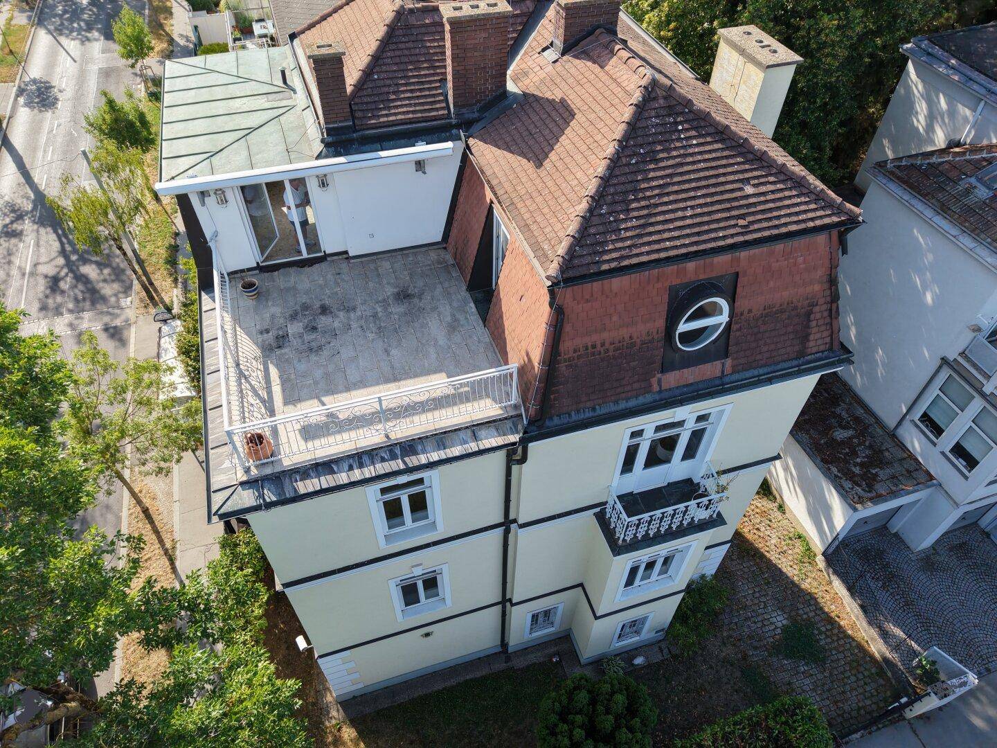 Panoramische Luftansicht des Anwesens, die die gelbe Fassade, das Mansarddach und die weitläufige Dachterrasse hervorhebt.
