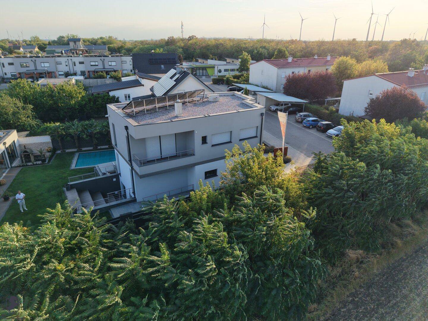 Panoramablick aus der Luft auf das moderne Anwesen mit Pool und Windrädern am Horizont.