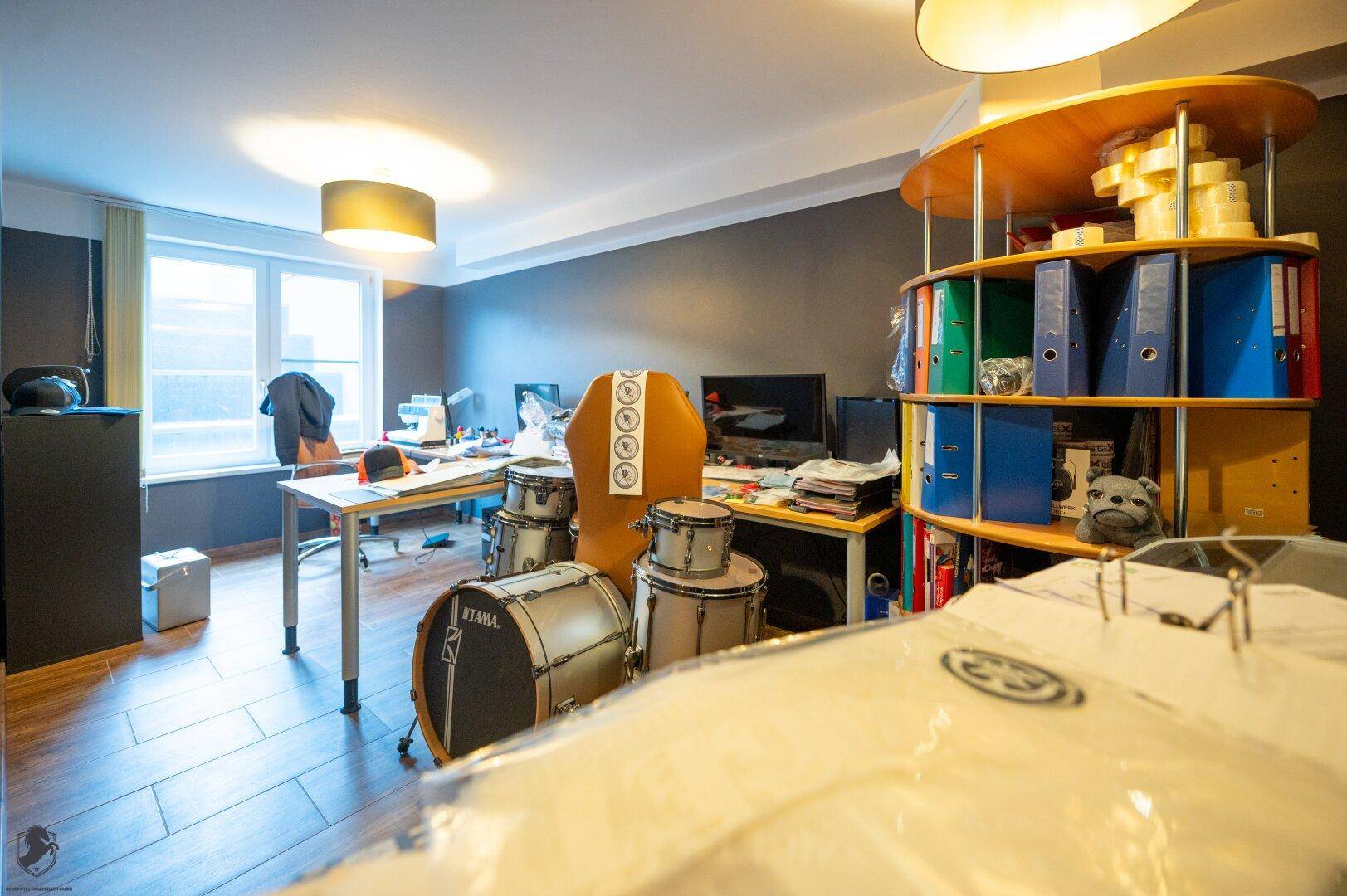 Vielseitiger Raum, eingerichtet als Büro und Musikstudio mit Schlagzeug und Regalen.