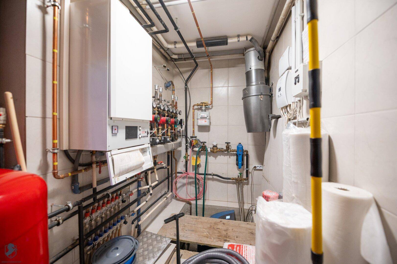 Technikraum mit Heizungsanlage, Warmwasserboiler und umfangreicher Rohrinstallation.