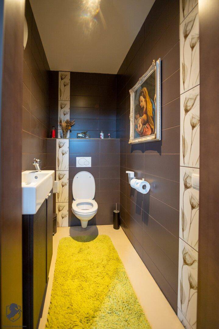 Stilvolles Gäste-WC mit dunklen Fliesen, wandhängender Toilette und modernem Waschbecken.