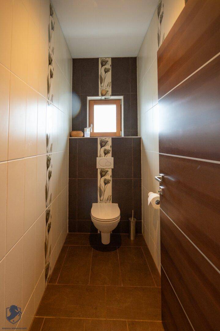 Helles Gäste-WC mit Fenster, modernen Fliesen und wandhängender Toilette.