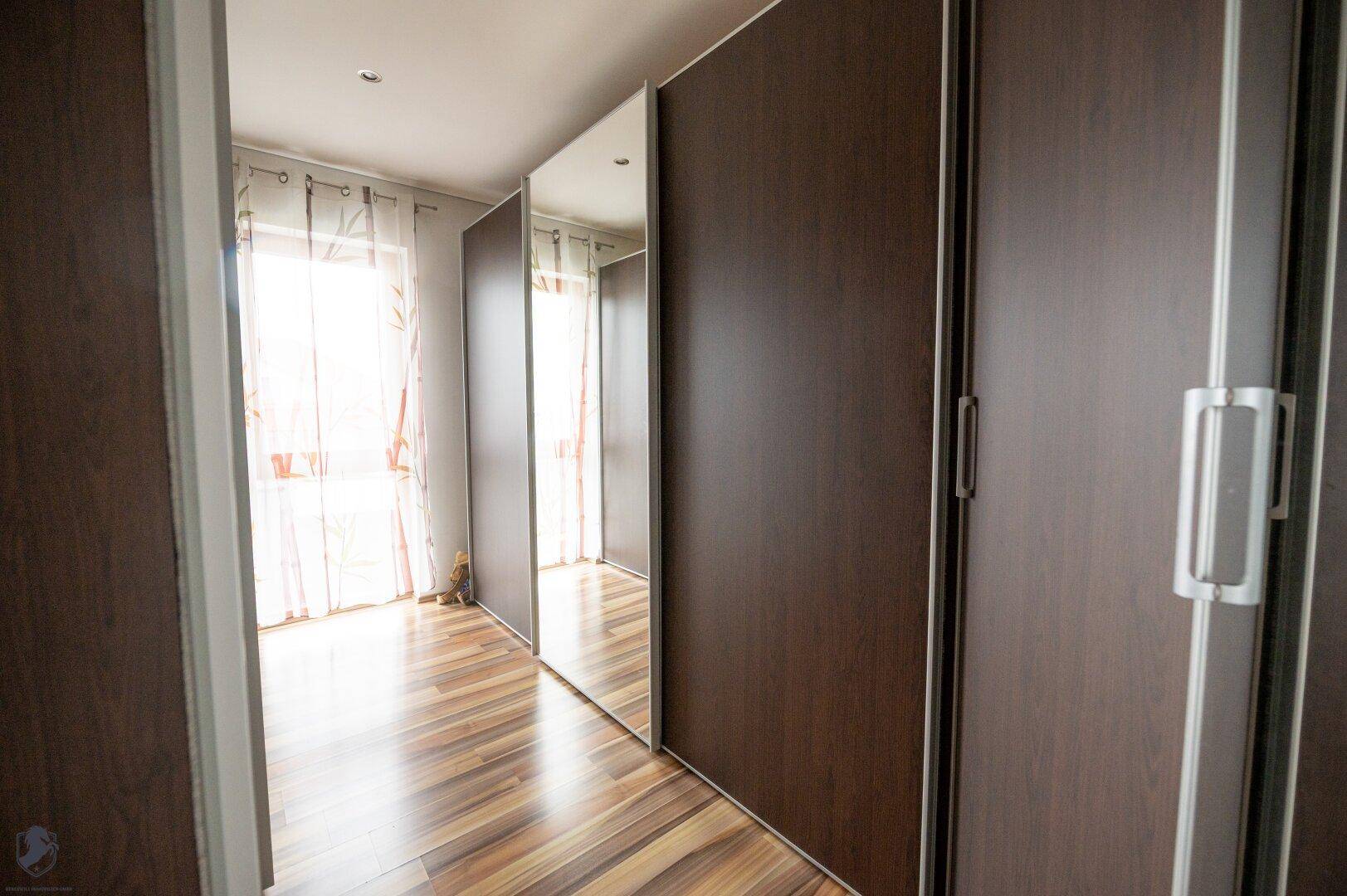 Praktischer begehbarer Kleiderschrank mit Spiegeltüren und Fenster für Tageslicht.