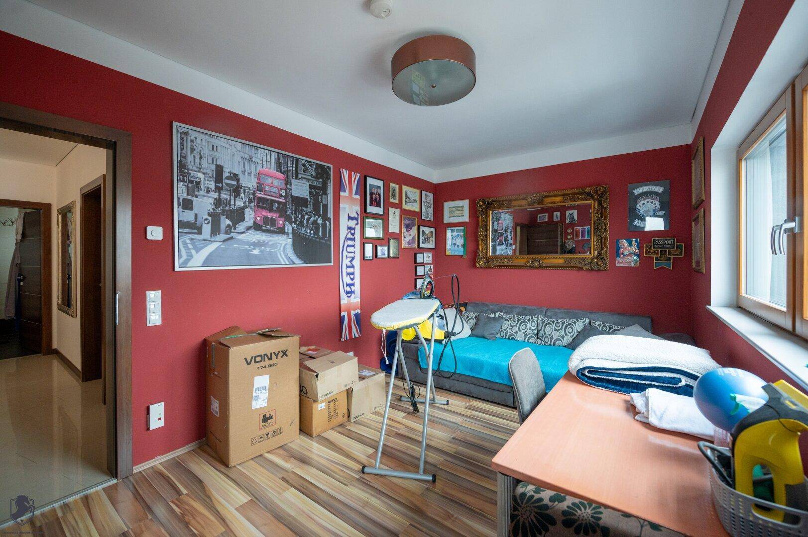 Farbenfrohes Wohnzimmer mit roten Wänden, Sofa und vielseitiger Nutzungsmöglichkeit.