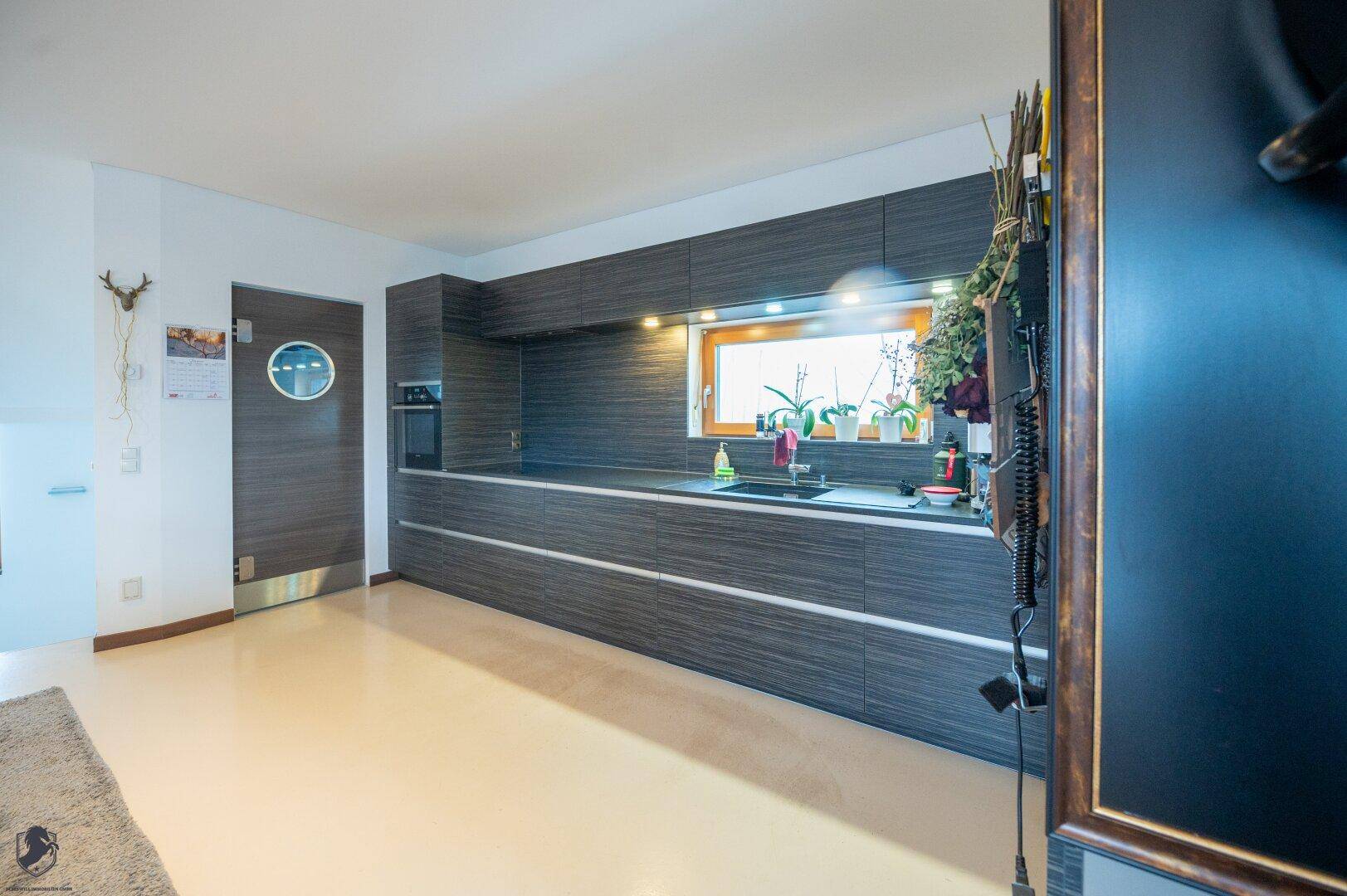 Moderne Küche mit dunklen Holzfronten, integriertem Backofen und einem Fenster über der Arbeitsfläche.