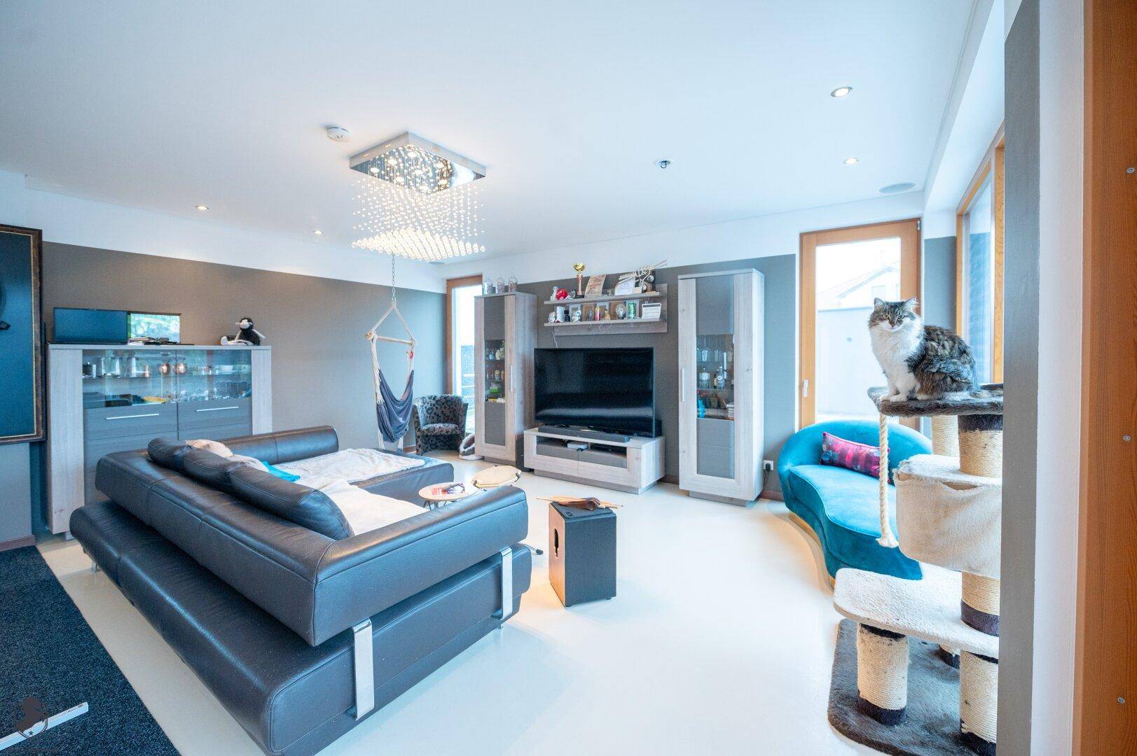 Helles Wohnzimmer mit großem Sofa, modernem TV-Möbel und raumhohen Fenstern, die den Raum lichtdurchfluten.
