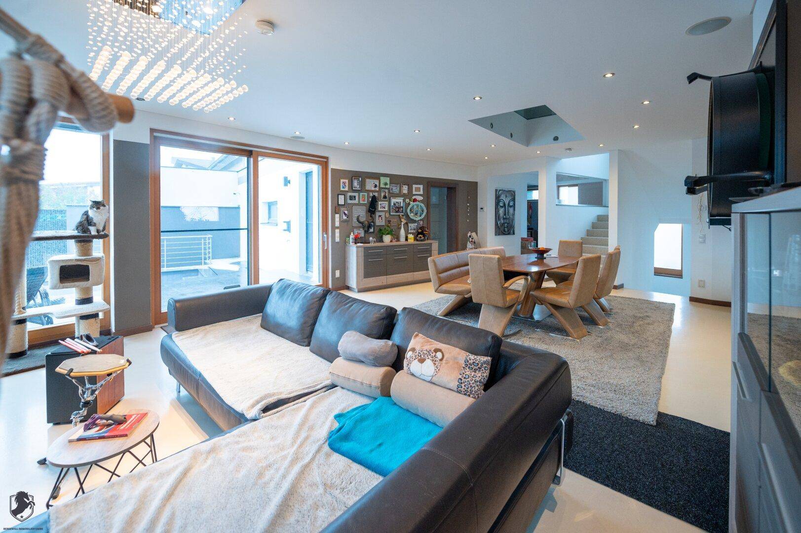 Wohnzimmer mit großem Sofa, Blick auf den Essbereich und Zugang zu einer Außenterrasse durch breite Schiebetüren.